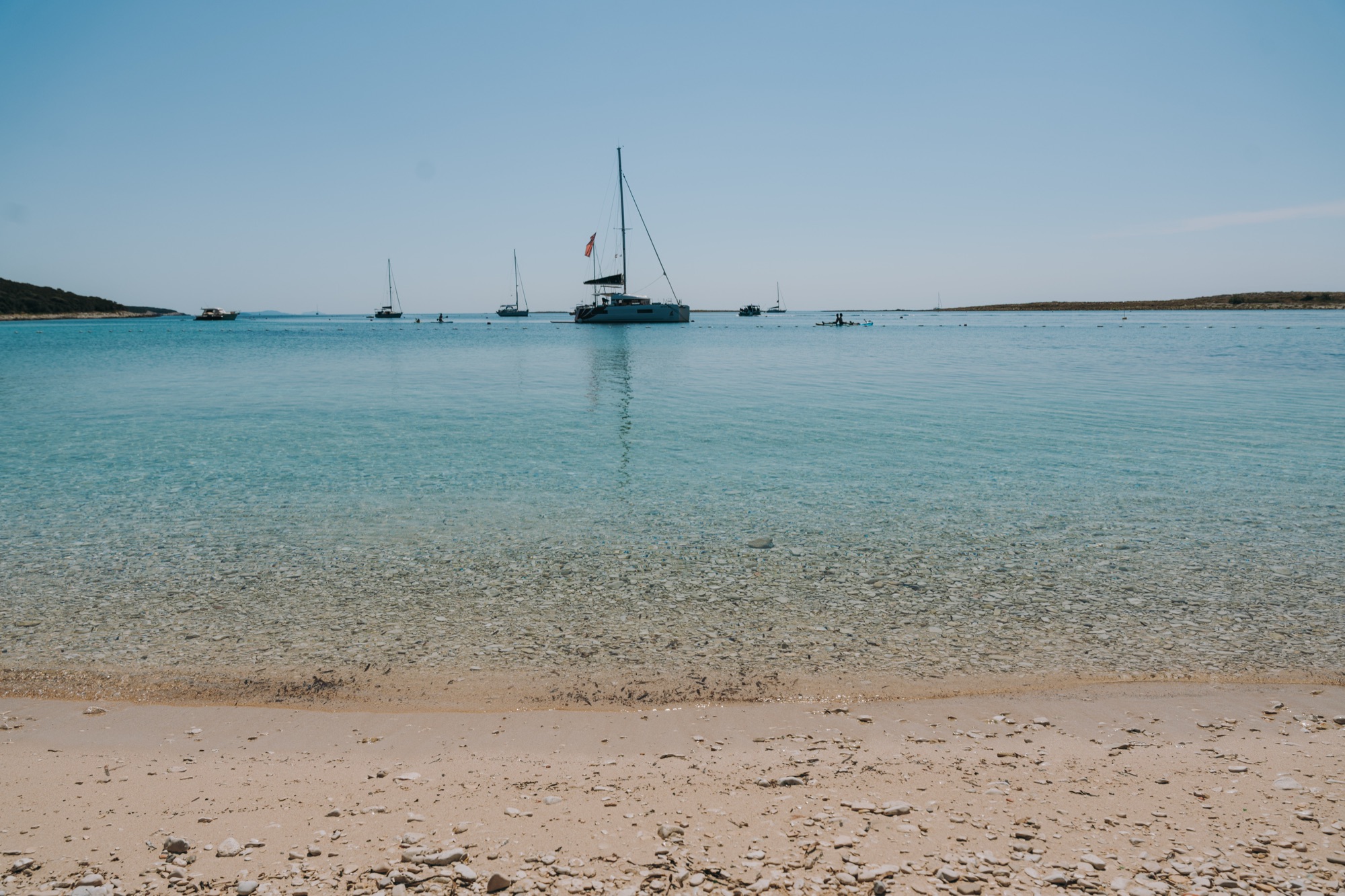 The sandy beach by the church on Premuda, with boats anchored in the shallow water