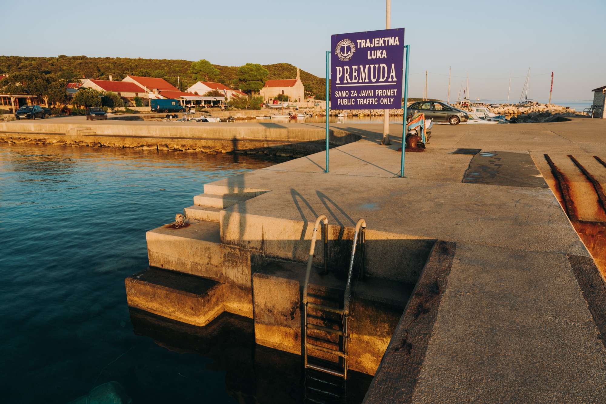 The ferry-port sign at Premuda in the evening light, the village and its church behind
